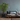A styled living room corner with a wooden bench, gray and blue-gray cushions, a potted green tree, a hanging lantern light, and a coffee table against a textured blue-gray wall.
