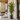 A tall artificial palm tree in a black geometric planter, placed on a modern outdoor patio next to a beige sectional sofa and stone fireplace.