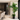 A tall artificial palm tree in a black pot, placed in a modern dining room next to a beige stone pillar.